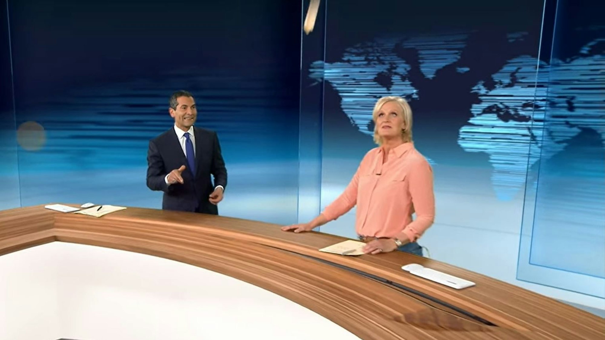 „heute“-Moderator Mitri Sirin beendete die Nachrichten-Sendung am 7. März 2023 mit einer fragwürdigen Aktion. Er warf einen Papierflieger durchs Studio. Kollegin Kristin Otto schaut verwirrt zu.