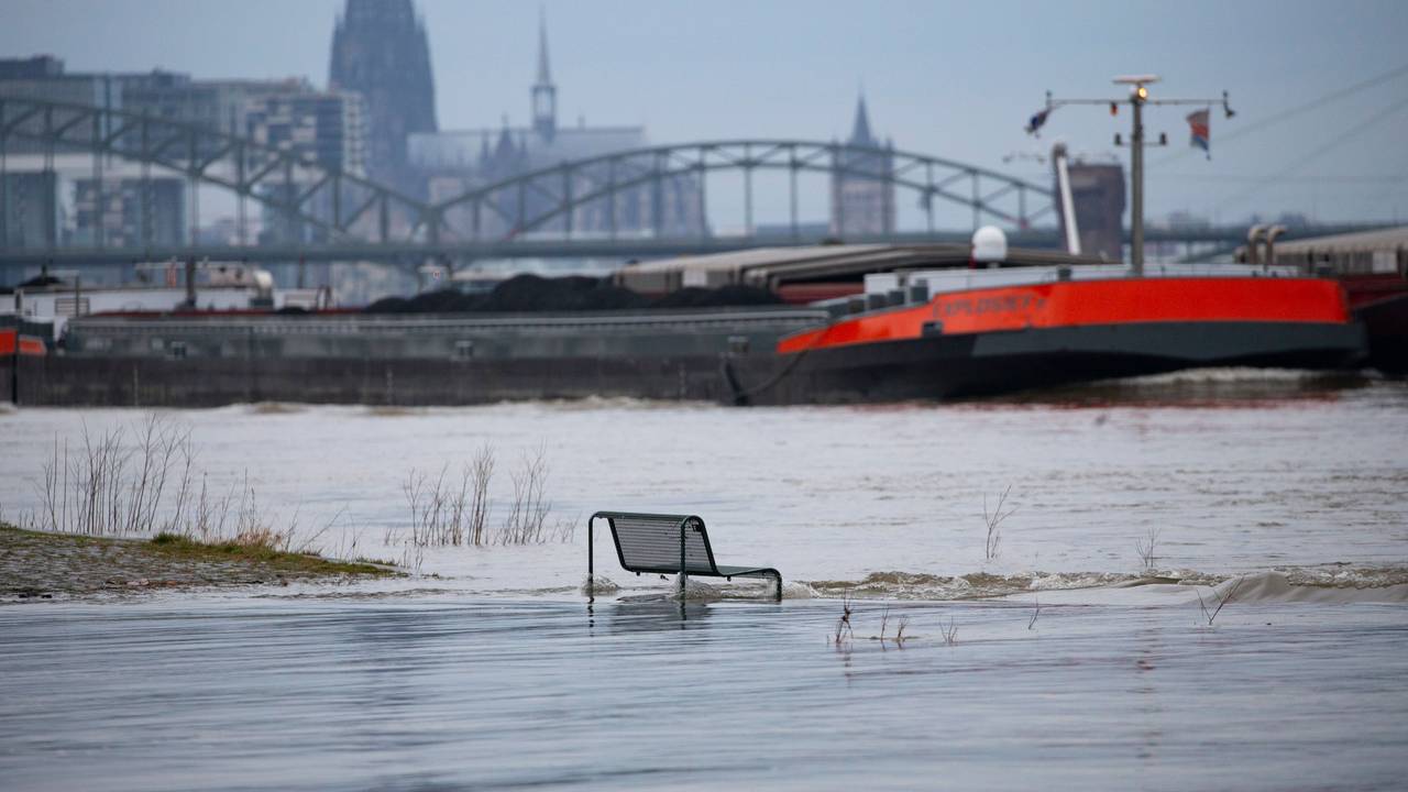 Binnenschiffe fahren auf dem Rhein vor der Kulisse des Kölner Doms, im Vordergrund steht eine vom Wasser umspülte Sitzbank. Noch hat der Kölner Pegel die Hochwassermarke nicht überschritten.