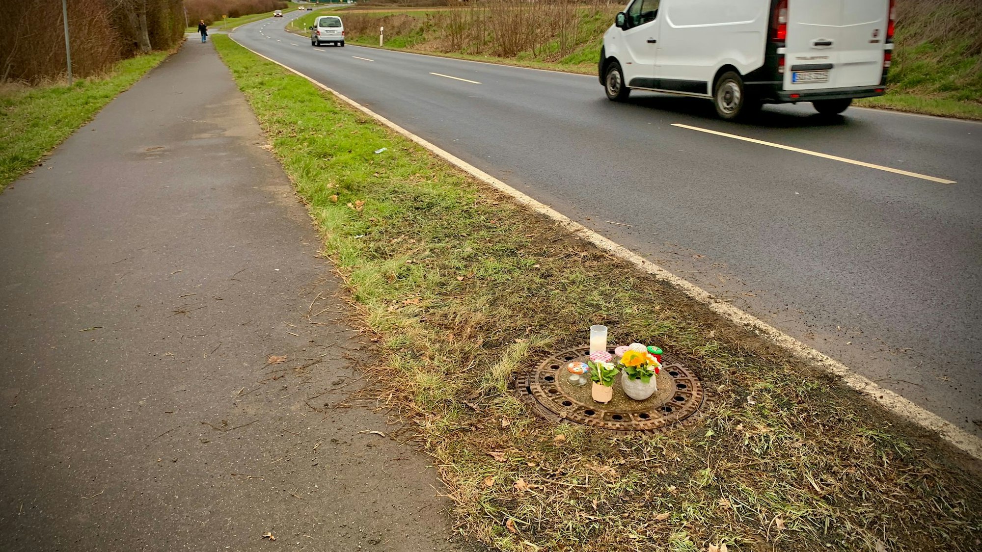Kerzen und Blumen stehen auf dem Gullydeckel, der sich an einer Straße befindet.