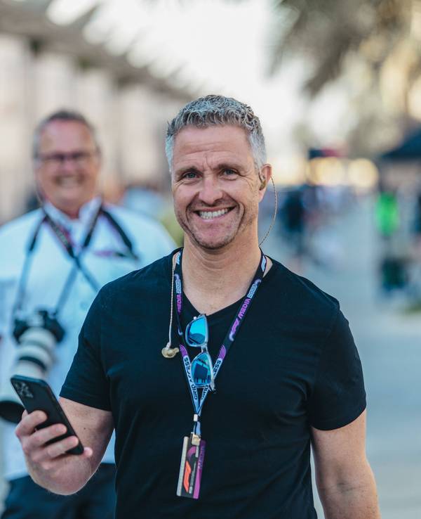 Ralf Schumacher hat sein Handy in der Hand und lächelt.