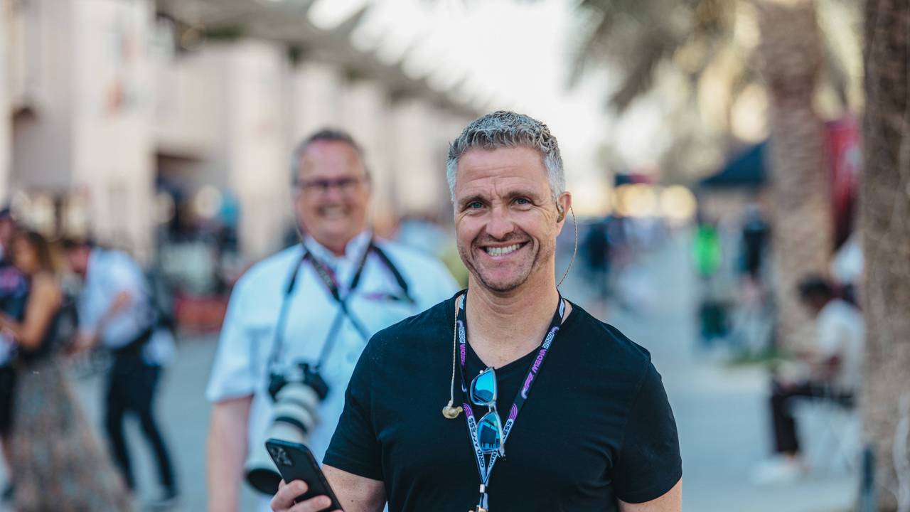 Ralf Schumacher hat sein Handy in der Hand und lächelt.