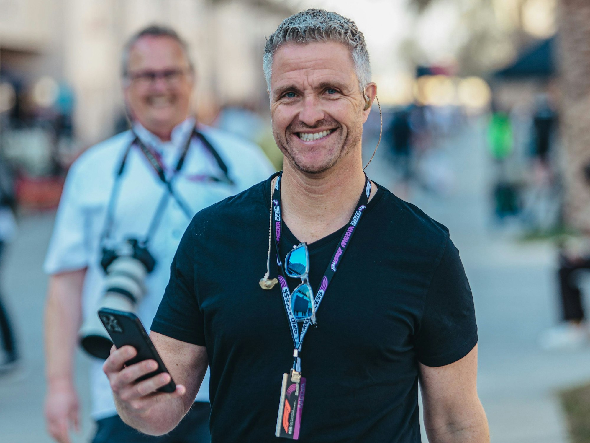 Ralf Schumacher hat sein Handy in der Hand und lächelt.