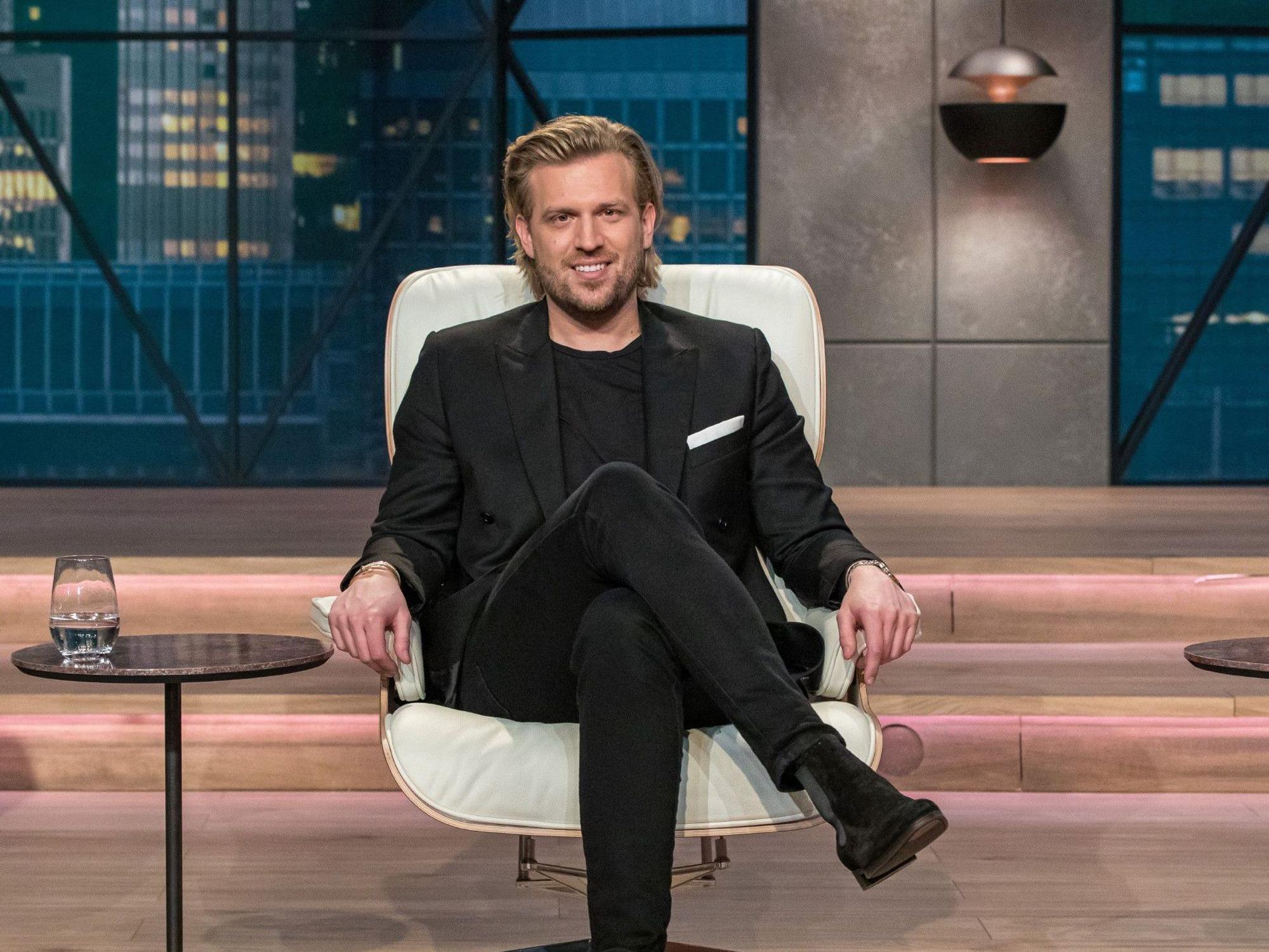 Investor Tillman Schulz sitzt auf einem Stuhl im Studio von Die Höhle der Löwen. Er trägt einen dunklen Anzug und ein dunkles T-Shirt. Die Verwendung des sendungsbezogenen Materials ist nur mit dem Hinweis und Verlinkung auf RTL+ gestattet.