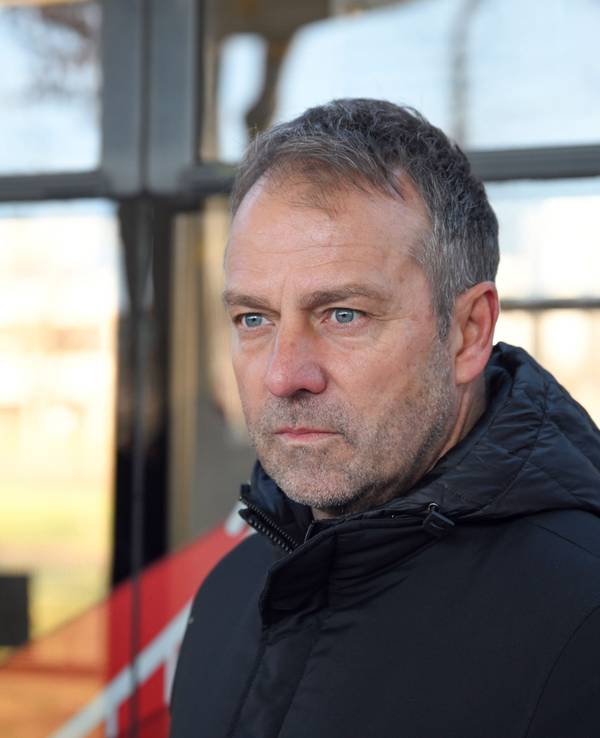 Fußball-Bundestrainer Hansi Flick steht vor einer Straßenbahn.