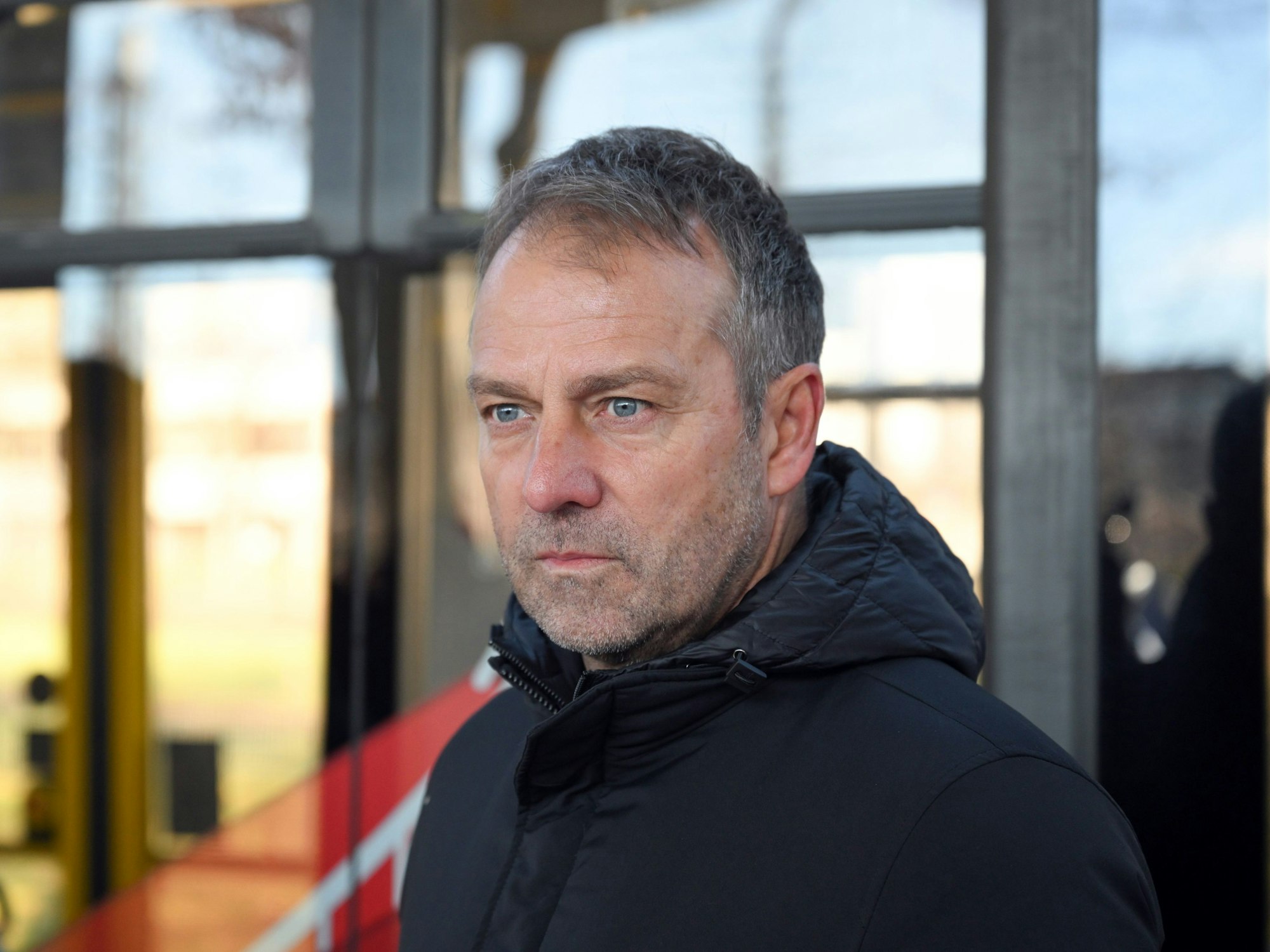 Fußball-Bundestrainer Hansi Flick steht vor einer Straßenbahn.