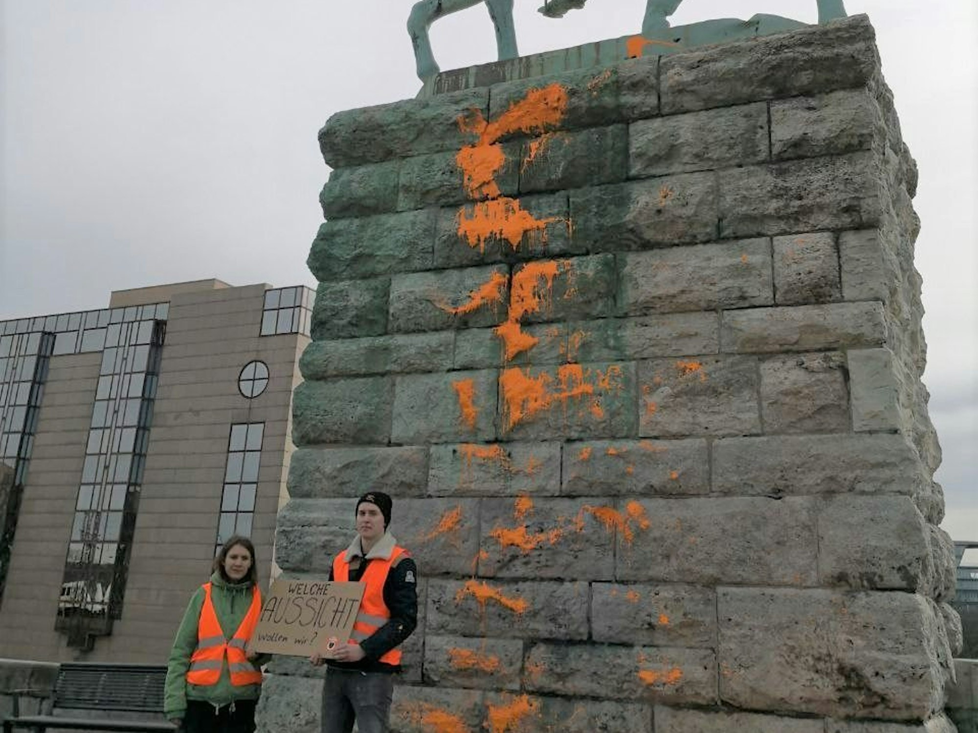 Eine junge Frau und ein junger Mann stehen vor dem Reiterstandbild an der Hohenzollnerbrücke, dessen Sockel mit Farbe beschmiert ist.