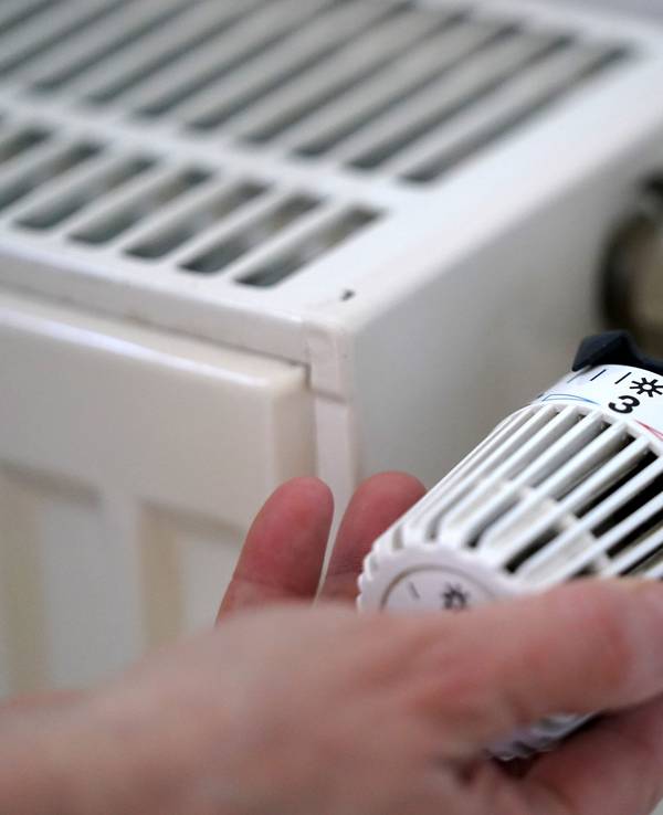 Eine Person dreht an einem Heizungsthermostat.