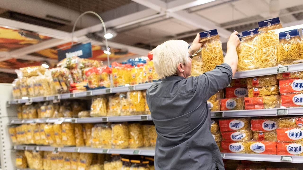 Das Symbolfoto aus dem Jahr 2020 zeigt eine Supermarkt-Mitarbeiterin mit grauem Hemd und kurzen blonden Haaren vor einem Regal mit allen möglichen Nudelsorten.
