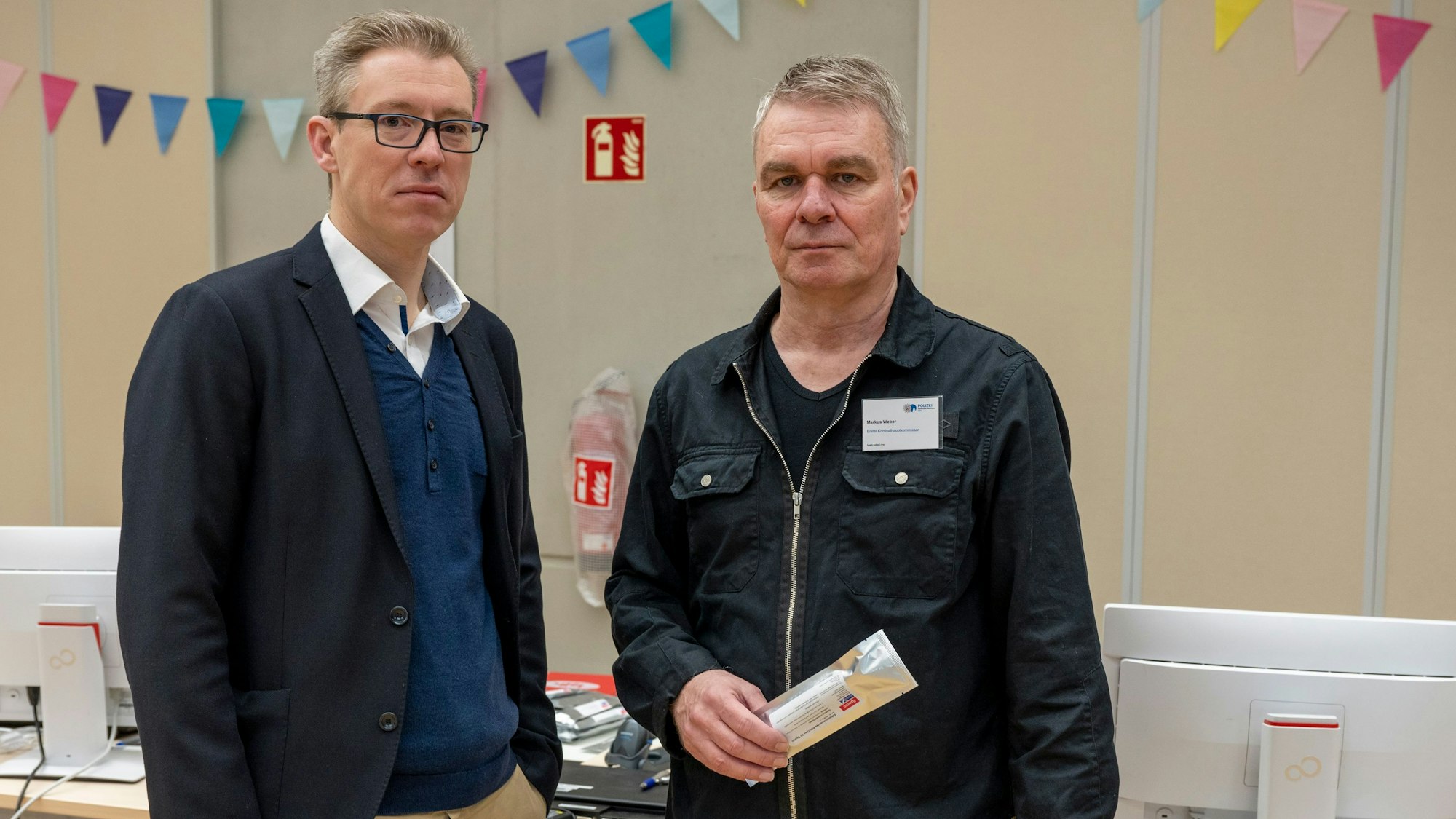 Oberstaatsanwalt Bastian Blaut und Kriminalhauptkomissar Markus Weber stehen in der Schulaula vor Tischen mit Computern.