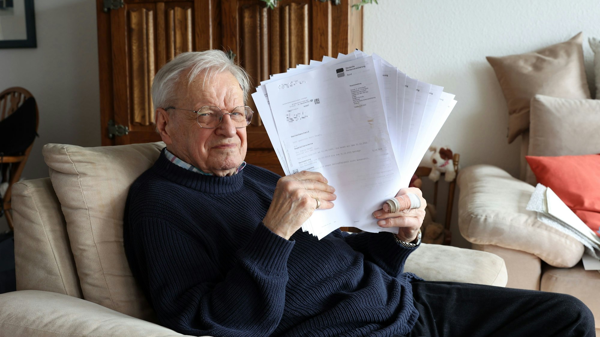 Ein Mann sitzt mit vielen Blättern Papier auf einem Sessel in seinem Wohnzimmer.