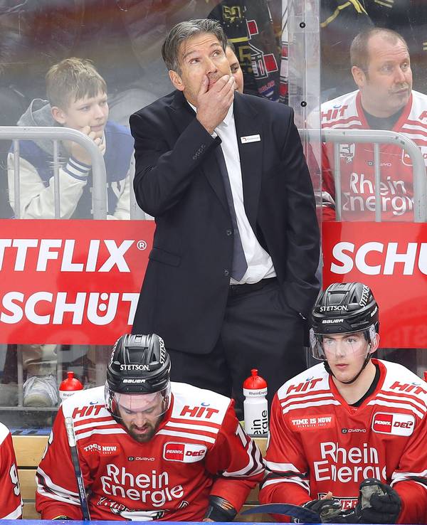 Eishockey-Playoffs in der DEL: Trainer Uwe Krupp, Headcoach der Kölner Haie, steht auf der Spielerbank und schaut angespannt nach oben auf die Anzeigetafel in der Lanxess-Arena.