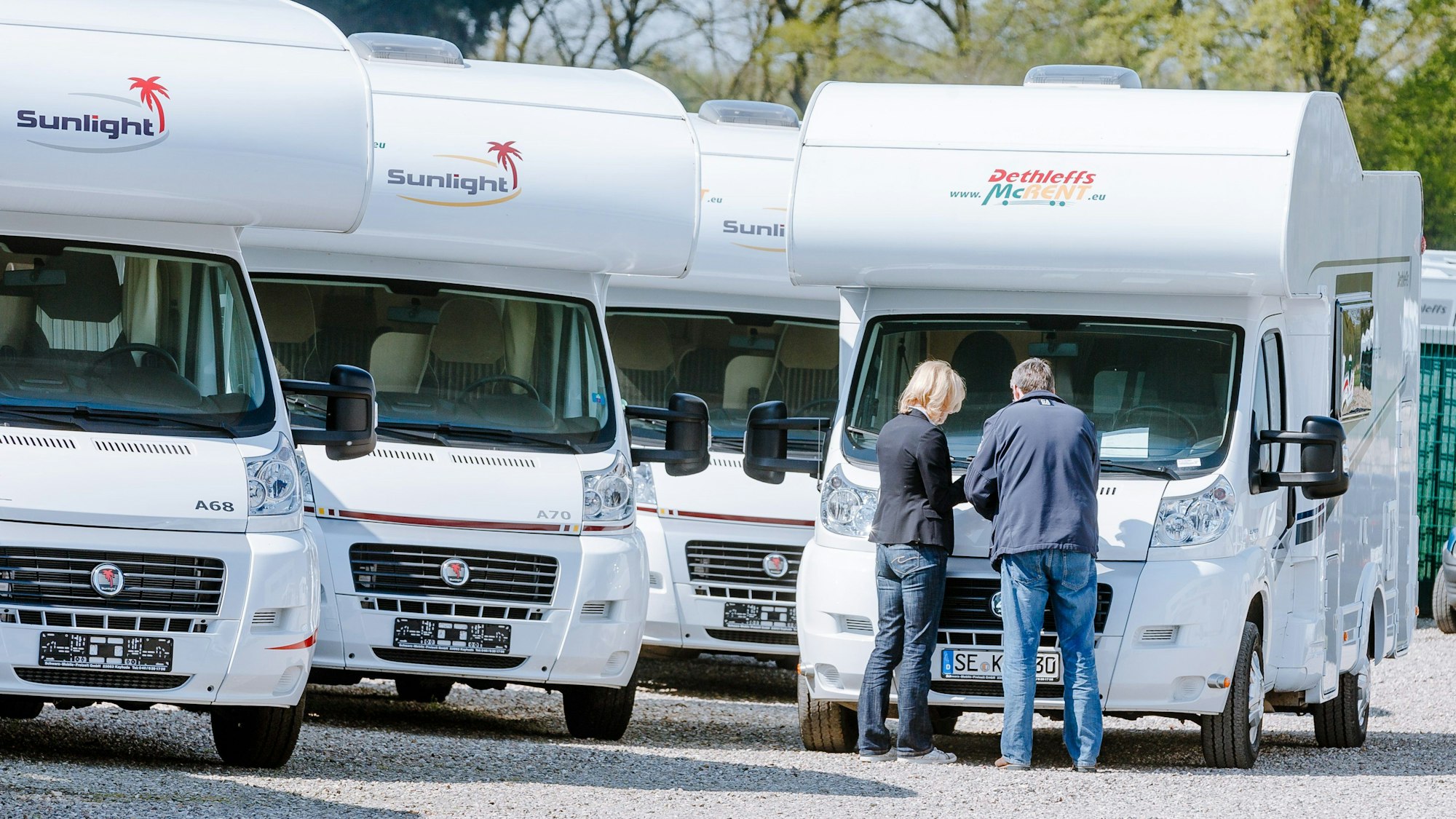 Ein Paar steht auf einem Parkplatz vor vier Wohnmobilen und vergleicht die Preise.