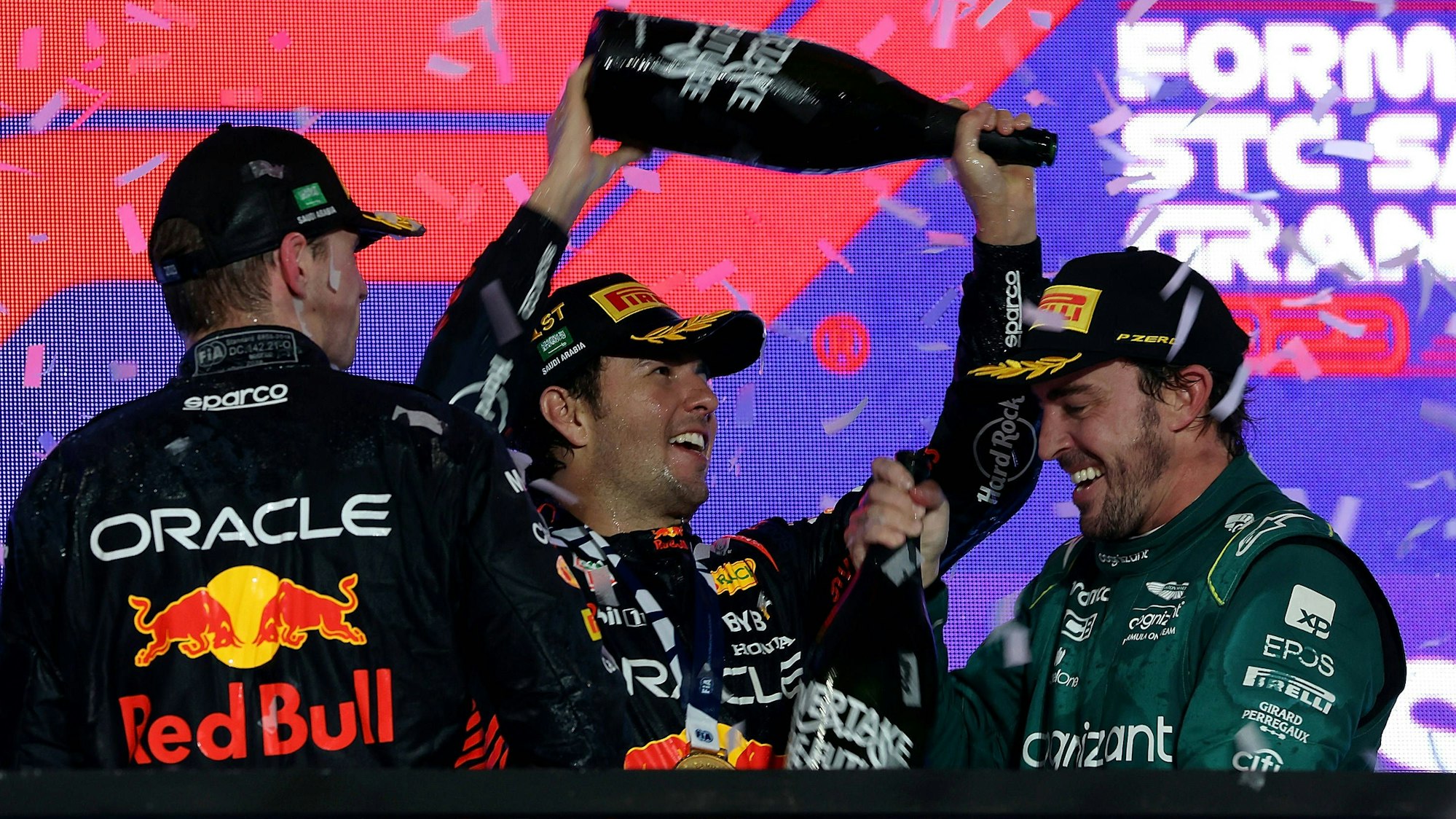 Sergio Perez schüttet Fernando Alonso Champagner über den Kopf, Max Verstappen schaut zu.