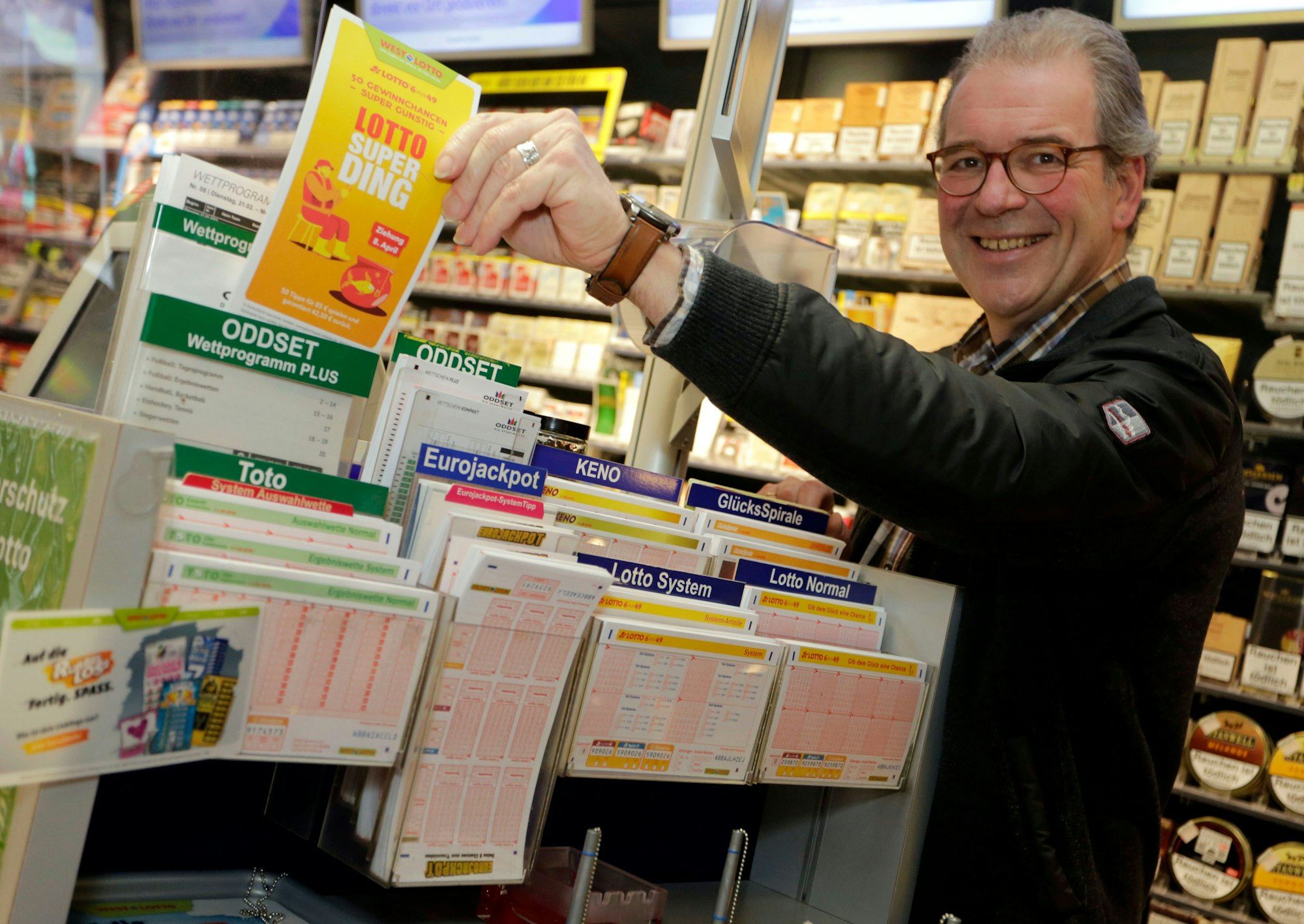 Mann steht im Kiosk am Lottostand und hält Superding Spielschein in der Hand.