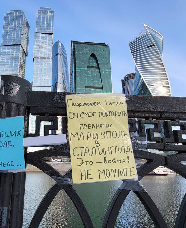 Zettel in den ukrainischen Nationalfarben (blau und gelb) hängen an der Brücke des Flusses Moskwa in Moskau. Im Hintergrund sind Gebäude des Hochhausviertels Moskwa City zu sehen.