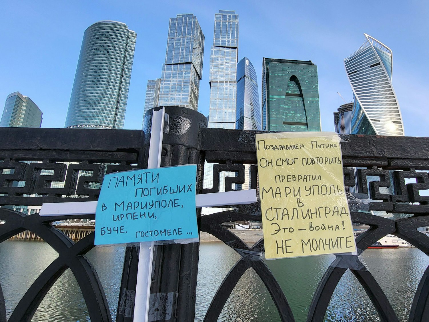 Zettel in den ukrainischen Nationalfarben (blau und gelb) hängen an der Brücke des Flusses Moskwa in Moskau. Im Hintergrund sind Gebäude des Hochhausviertels Moskwa City zu sehen.