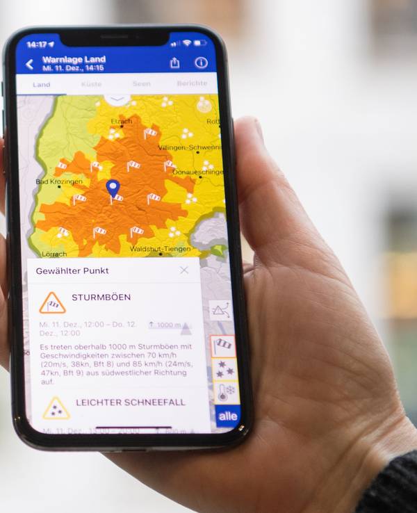 Das Symbolfoto aus dem Jahr 2019 zeigt eine Hand, die ein Smartphone hält. Auf dem Bildschirm sieht man eine Wetterkarte in gelb-orange, darunter steht Text.