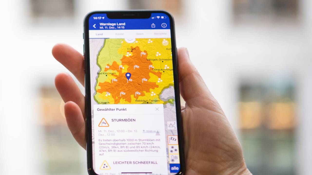 Das Symbolfoto aus dem Jahr 2019 zeigt eine Hand, die ein Smartphone hält. Auf dem Bildschirm sieht man eine Wetterkarte in gelb-orange, darunter steht Text.