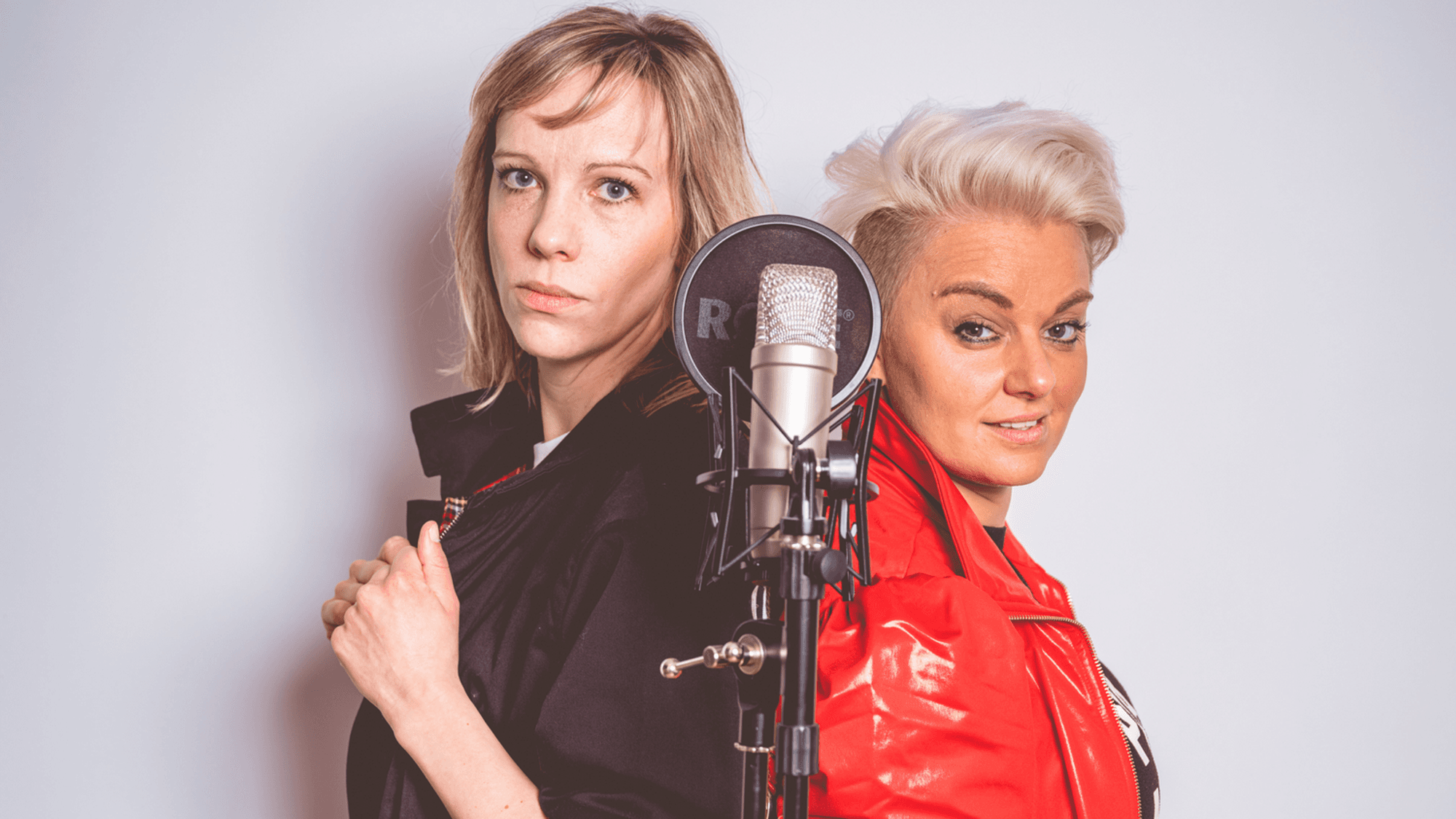Sophie Gesthuysen (l.) und Nicole Kempermann stehen vor einem Mikrofon und schauen über die Schulter in die Kamera.