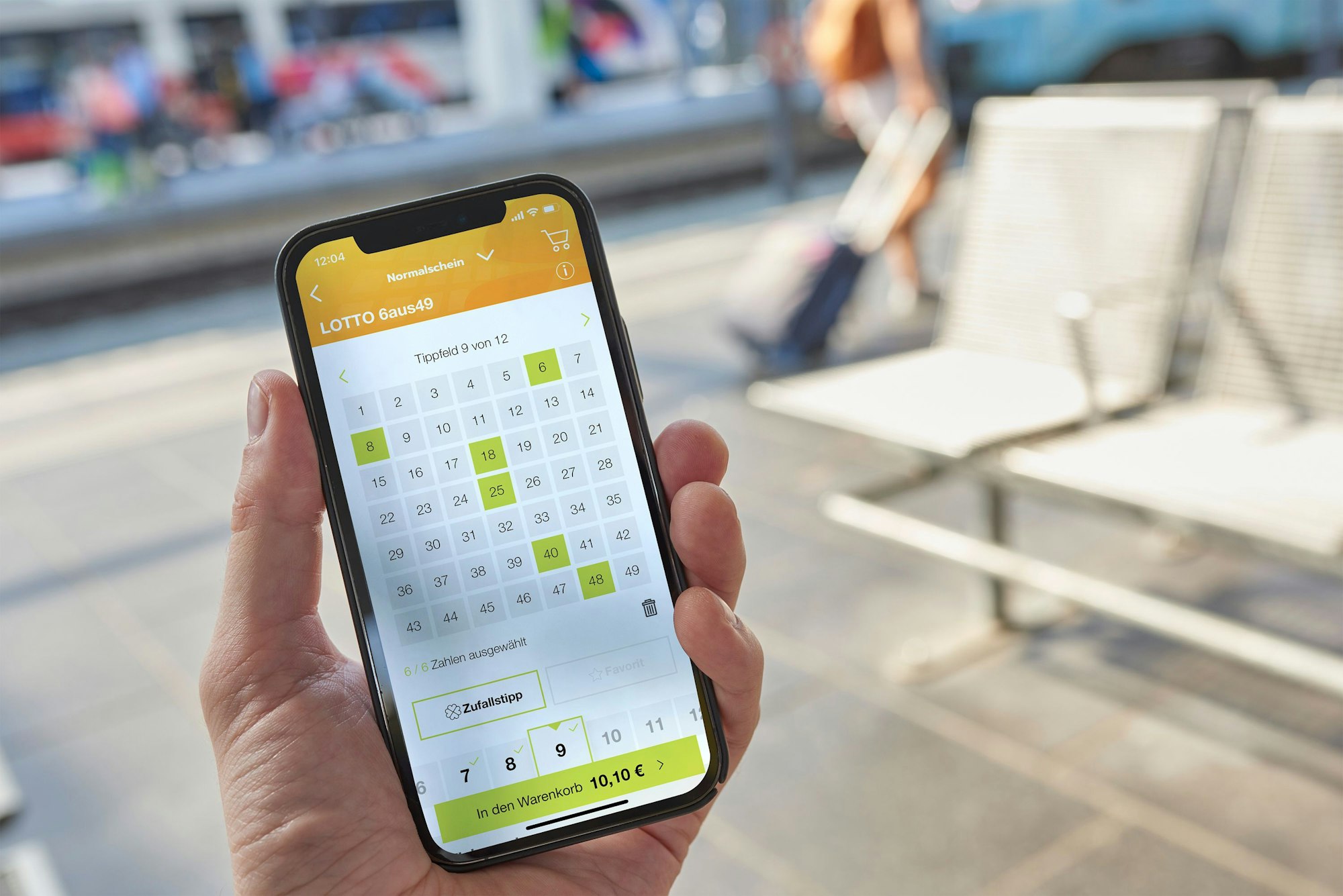 Mann hält Smartphone mit Lotto 6aus49 auf dem Display.