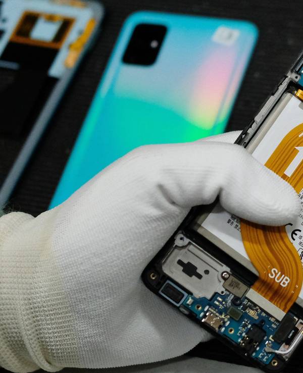 Das Bild zeigt eine Person in weißen Handschuhen, die ein defektes Smartphone repariert.