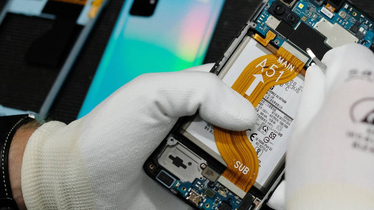 Das Bild zeigt eine Person in weißen Handschuhen, die ein defektes Smartphone repariert.