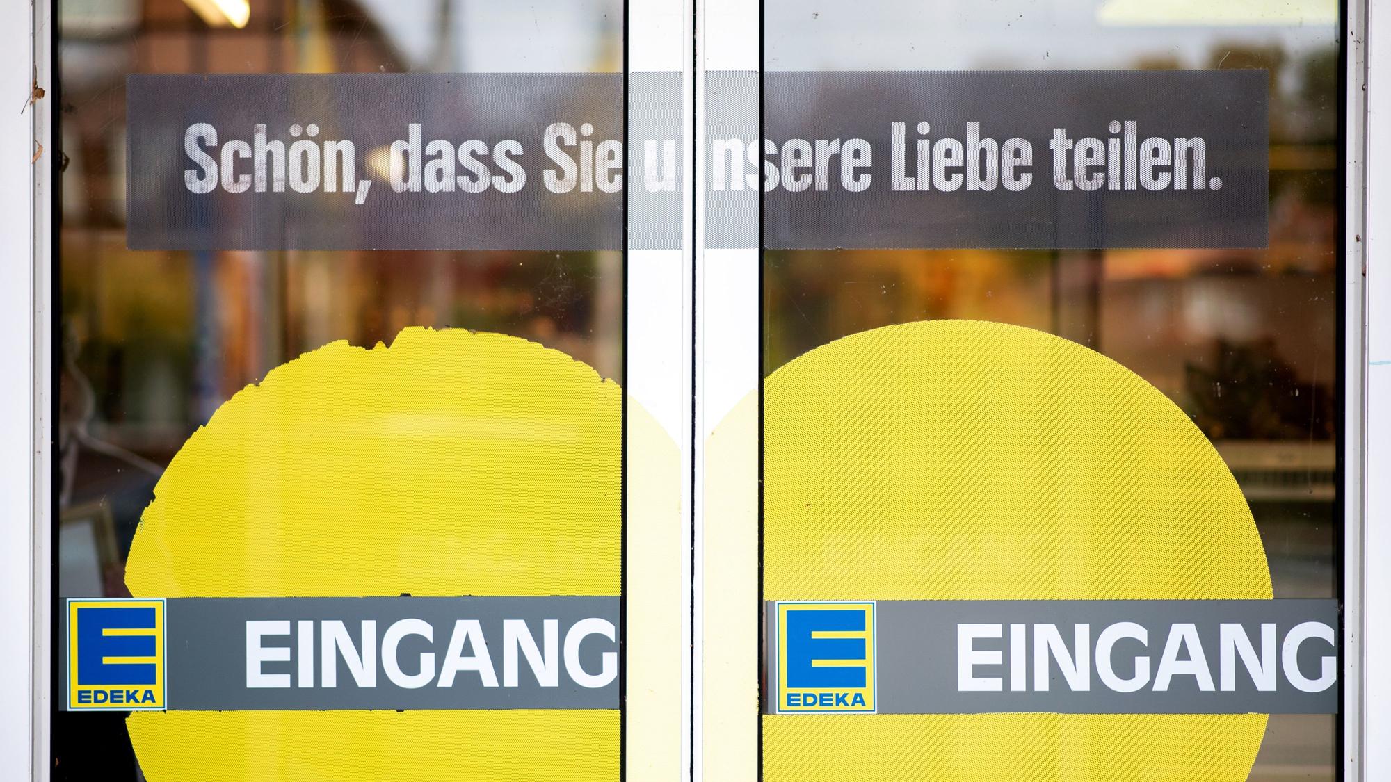 Das Symbolfoto aus dem Jahr 2020 zeigt die Eingangstüren einer Edeka-Filiale. Auf das Glas sind ein gelbes Herz, das Edeka-Logo sowie die Schriftzüge „Eingang“ und „Schön, dass Sie unsere Liebe teilen.“ gedruckt.