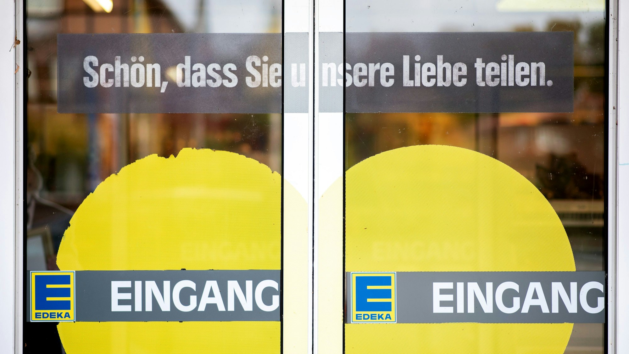 Das Symbolfoto aus dem Jahr 2020 zeigt die Eingangstüren einer Edeka-Filiale. Auf das Glas sind ein gelbes Herz, das Edeka-Logo sowie die Schriftzüge „Eingang“ und „Schön, dass Sie unsere Liebe teilen.“ gedruckt.