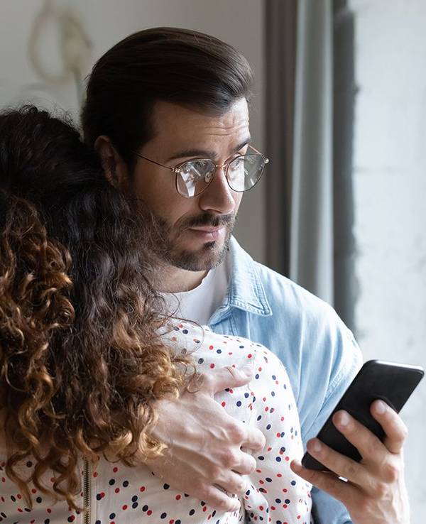 Mann hält Frau im Arm und schaut auf sein Handy