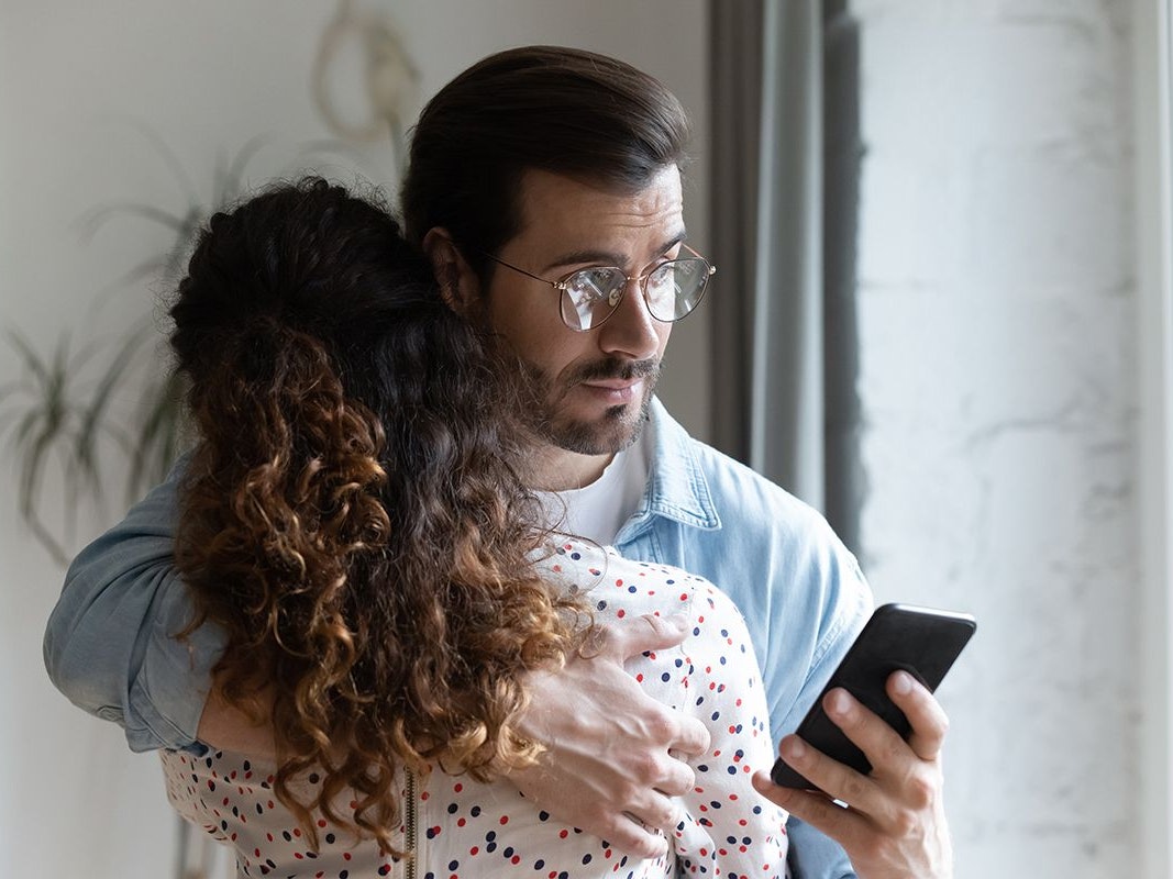 Mann hält Frau im Arm und schaut auf sein Handy