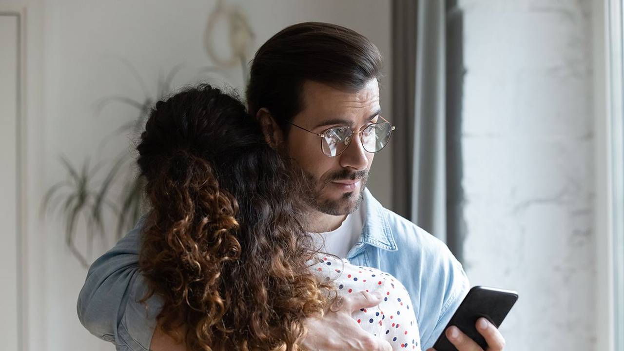 Mann hält Frau im Arm und schaut auf sein Handy