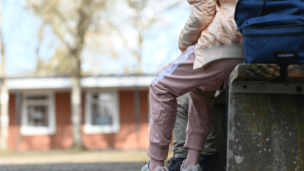 Eine Schülerin sitzt in einer Jogginghose auf dem Schulhof einer Schule.