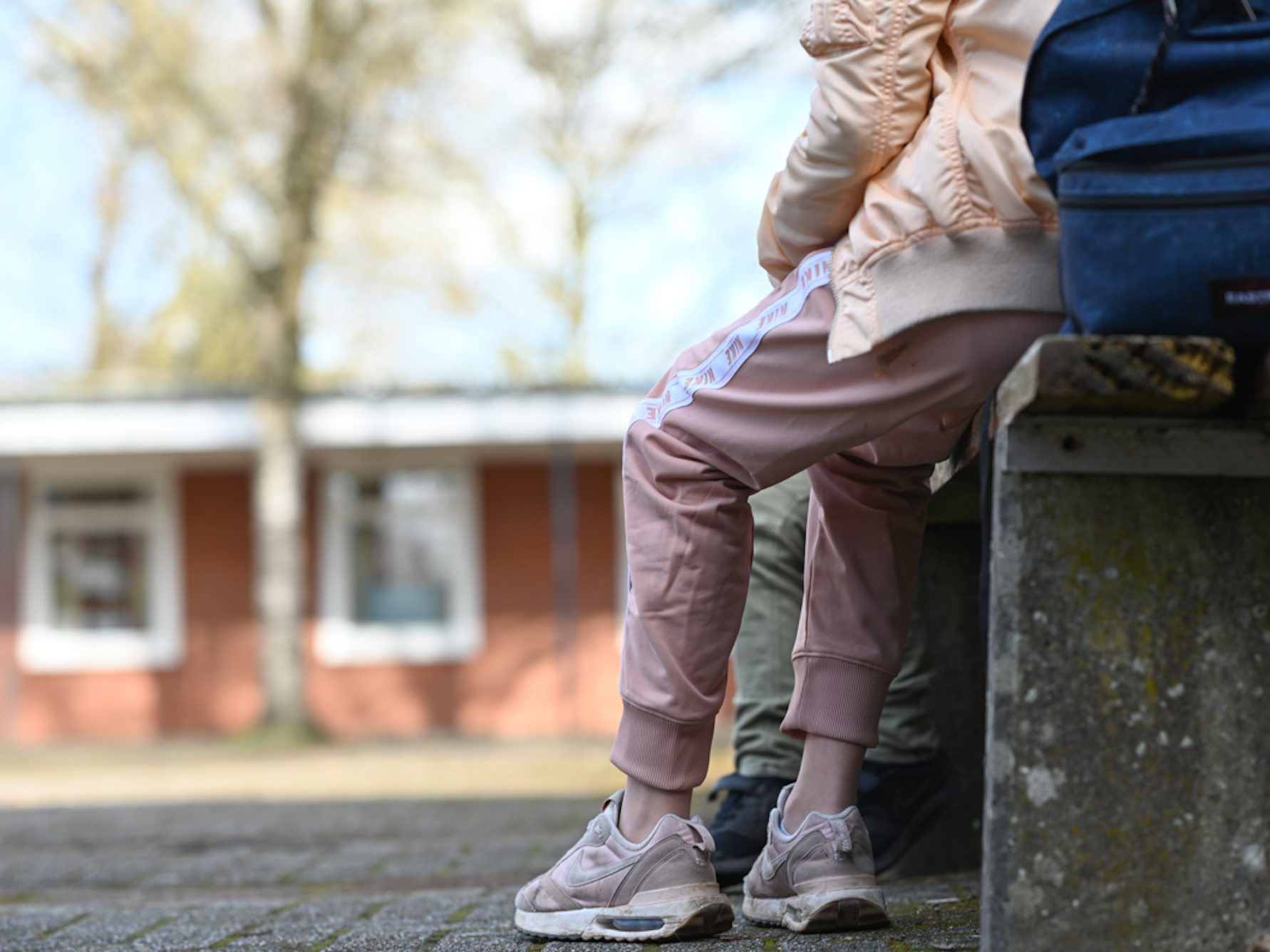 Eine Schülerin sitzt in einer Jogginghose auf dem Schulhof einer Schule.
