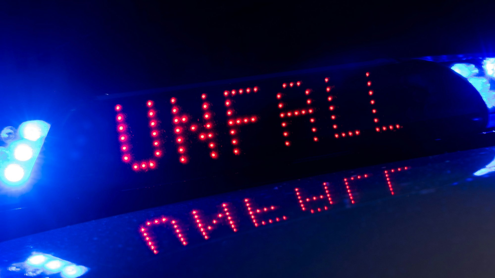 Das Blaulicht auf einem Fahrzeug der Polizei leuchtet in der Dunkelheit, während auf dem Display der Hinweis „Unfall“ zu lesen ist.