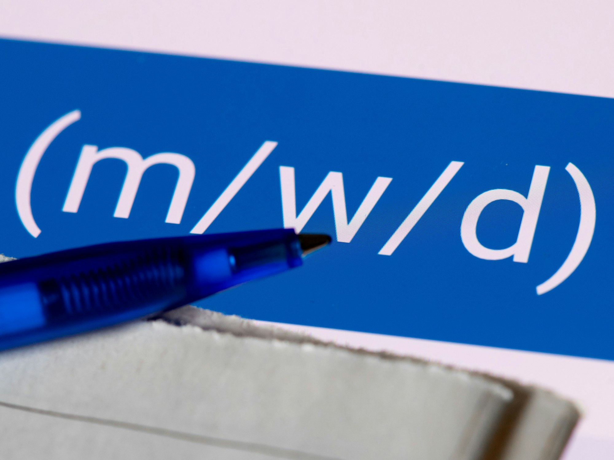 Eine Stellenanzeige mit den Abkürzungen m/w/d (männlich, weiblich, divers) ist auf einem Tablet zu sehen. Im Vordergrund liegen eine Tageszeitung und ein Stift.