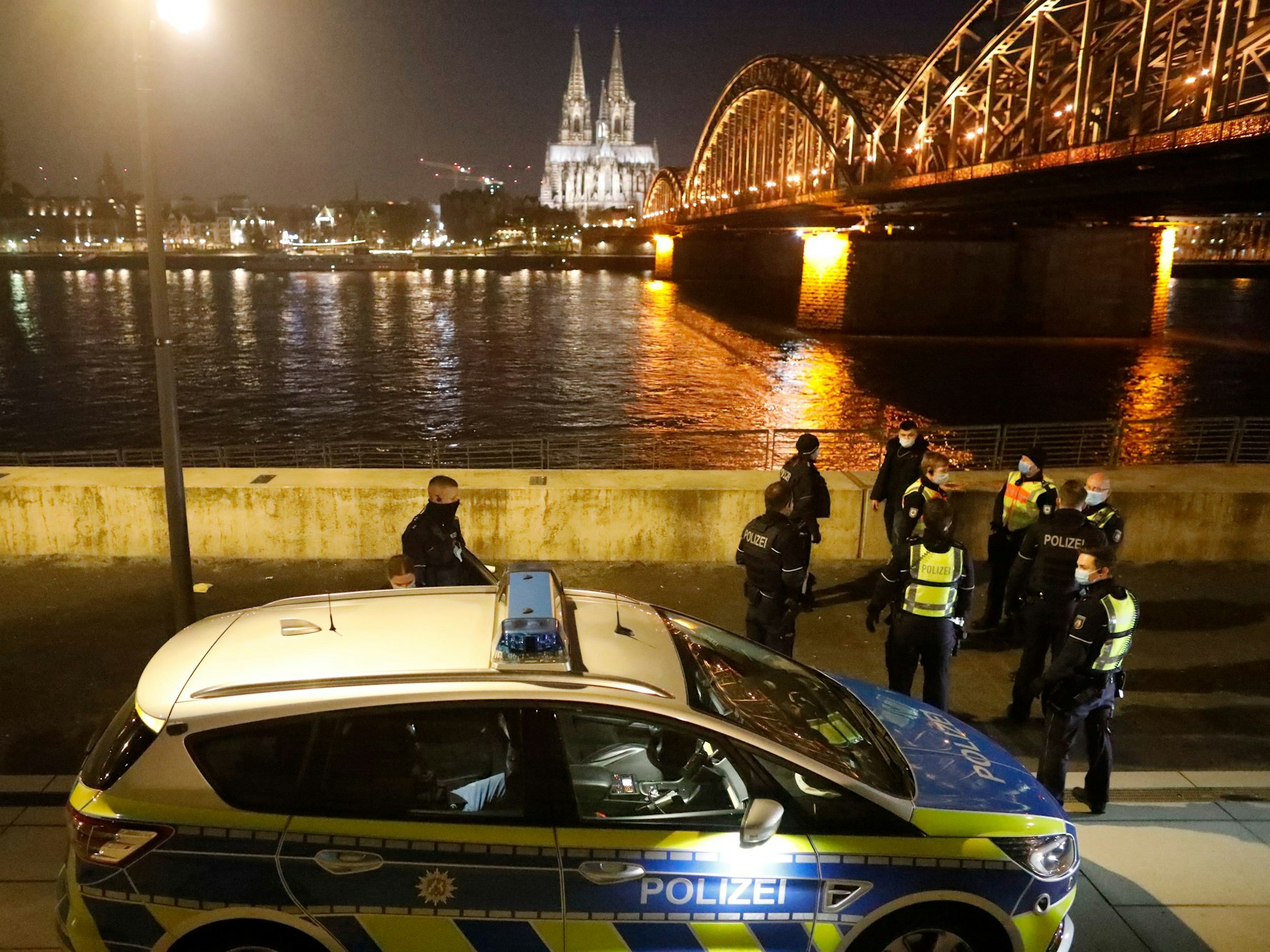 Polizeibeamte stehen mit einem Einsatzfahrzeug am Rheinufer in Deutz.