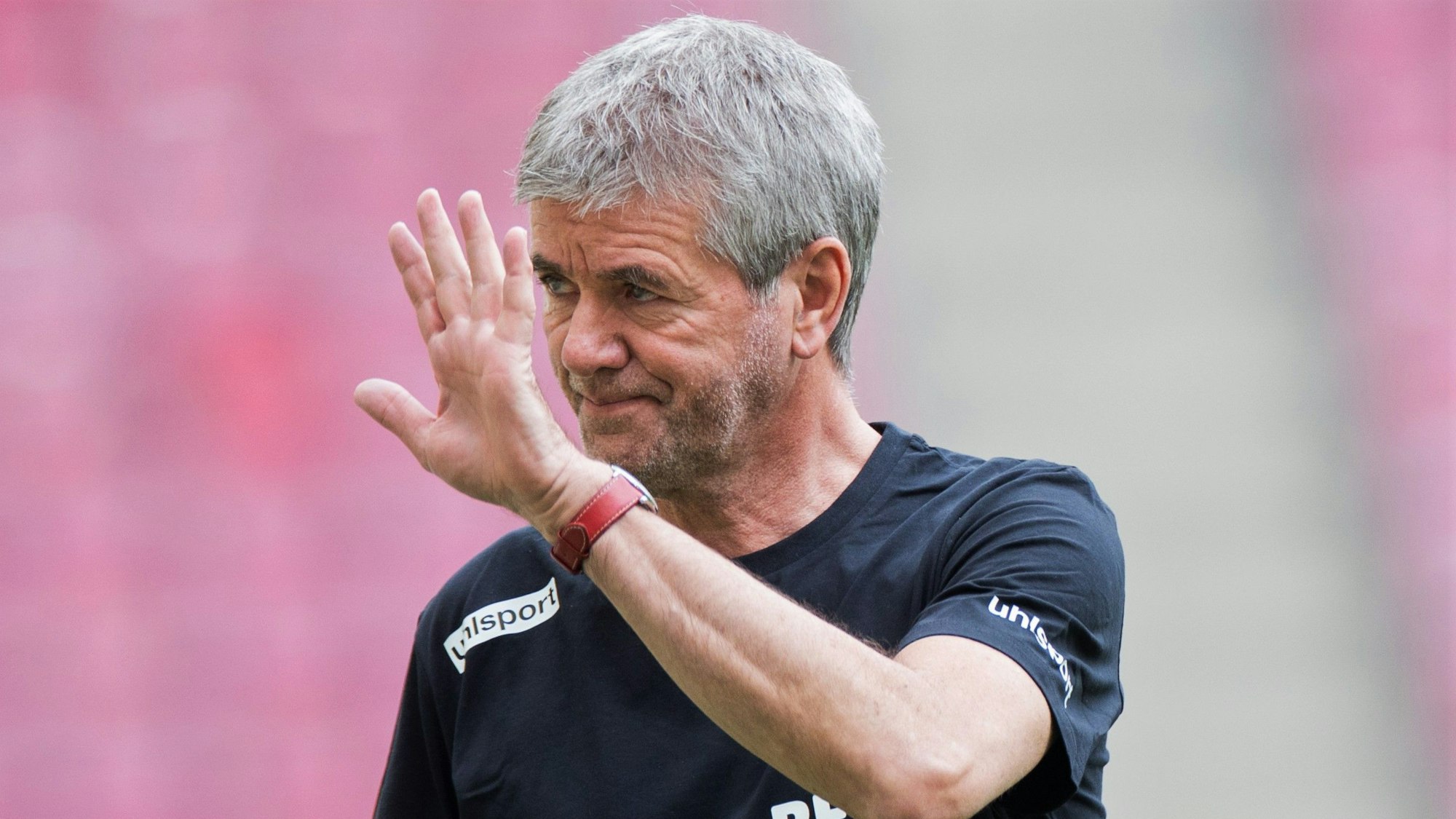 Friedhelm Funkel winkt bei einem Spiel des 1. FC Köln aus dem Innenraum Richtung Tribüne.