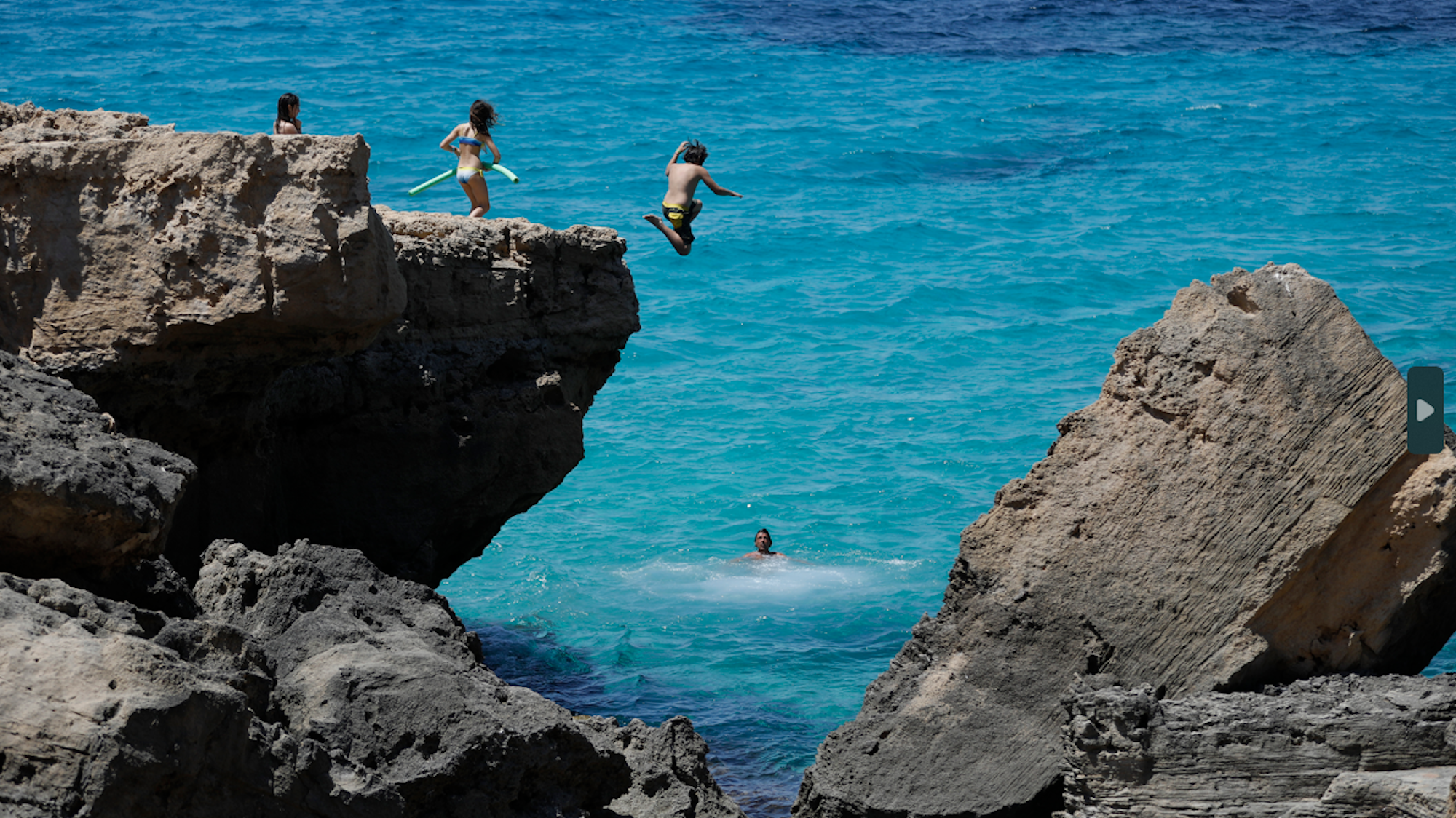 Menschen springen von einem Felsvorsprung in das Meer.