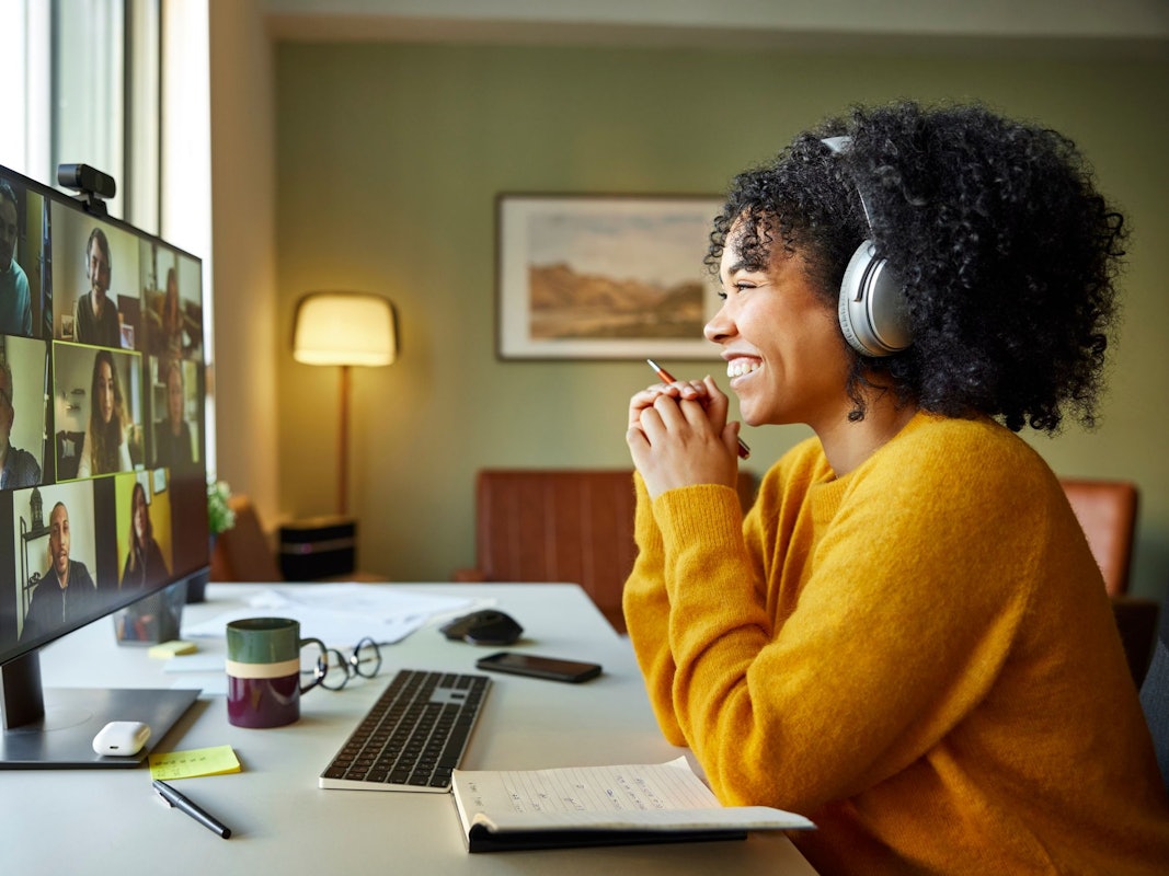Businesswoman with headphones smiling during video conference. Multiracial male and female professionals are attending online meeting. They are discussing business strategy.
