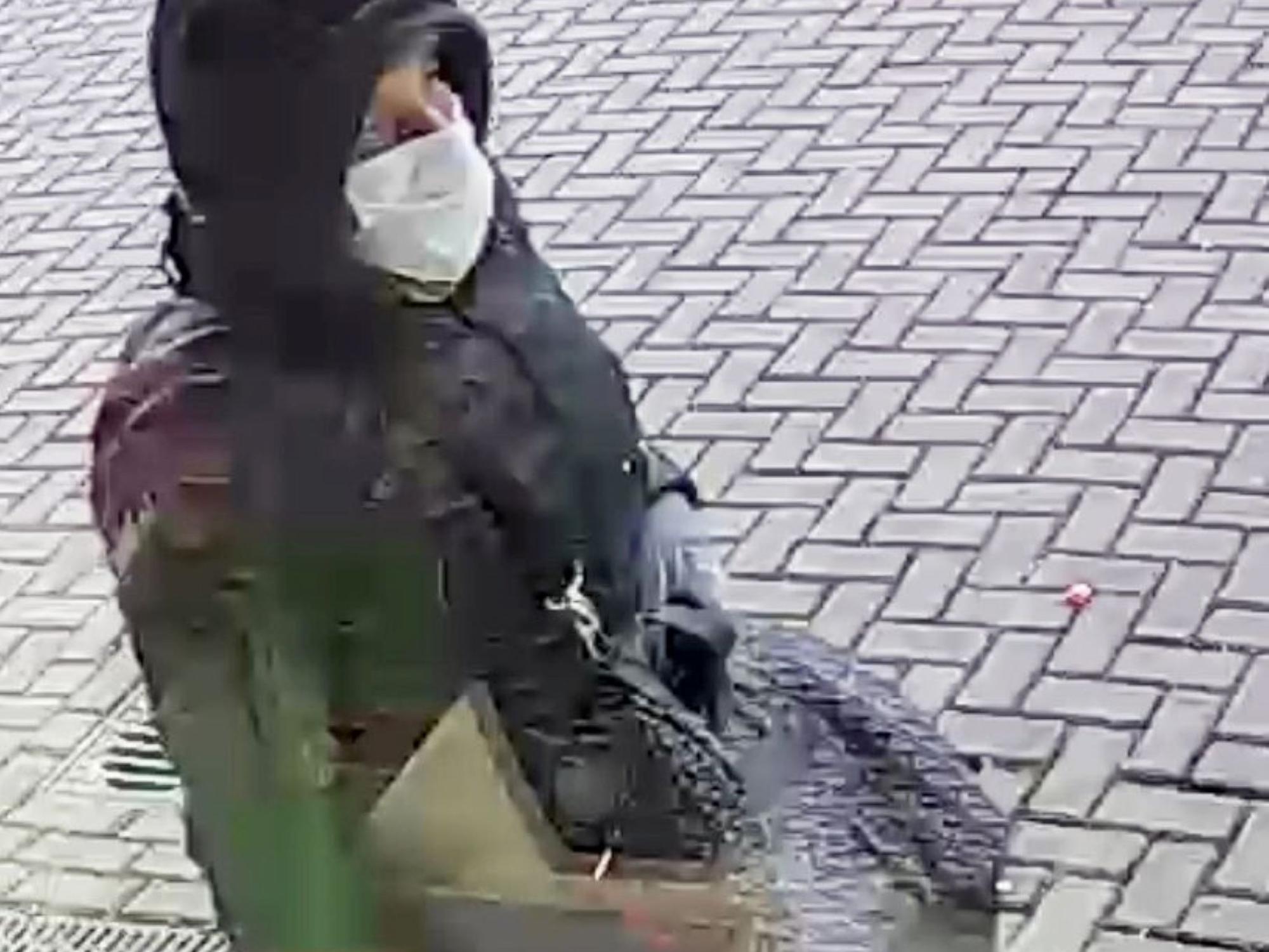Ein Mann hat eine Kapuze über den Kopf gezogen, er trägt einen Mund-Nasen-Schutz und eine Umhängetasche.