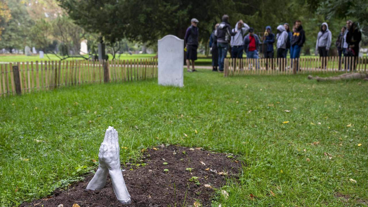 Das Symbolfoto aus dem Jahr 2022 zeigt ein frisches Grab auf einer grünen Wiese. Aus der Erde ragen zwei steinerne Hände, die zum Gebet aneinandergelehnt sind.