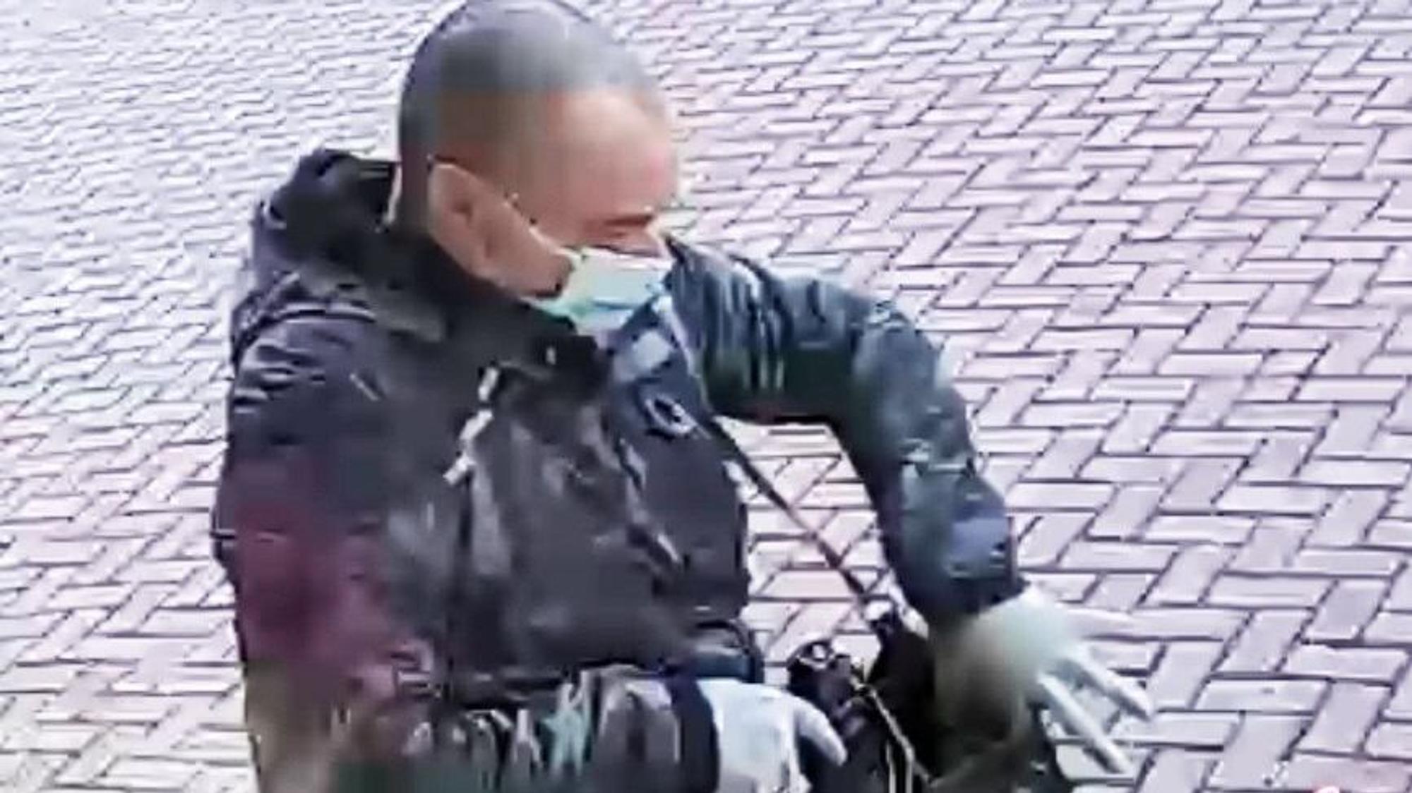 Ein Mann mit auffallend kurzen Haaren steckt einen Gegenstand, offenbar eine Waffe, in eine Umhängetasche.