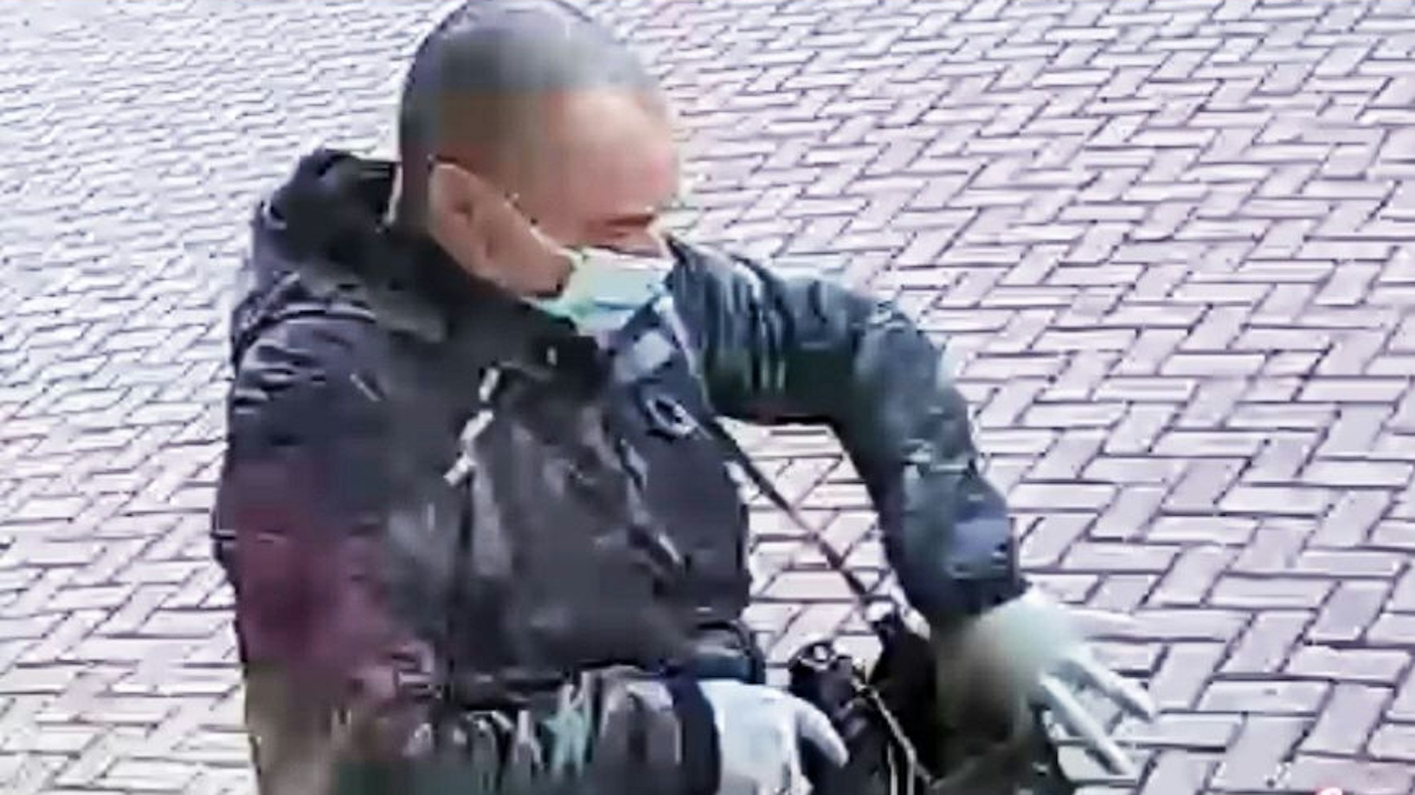 Ein Mann mit auffallend kurzen Haaren steckt einen Gegenstand, offenbar eine Waffe, in eine Umhängetasche.