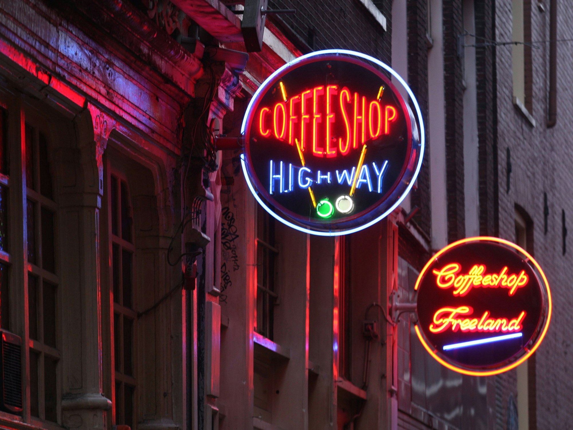 Das Foto zeigt zwei beleuchtete Neon-Schilder von Coffeeshops im Rotlichtviertel Amsterdams.