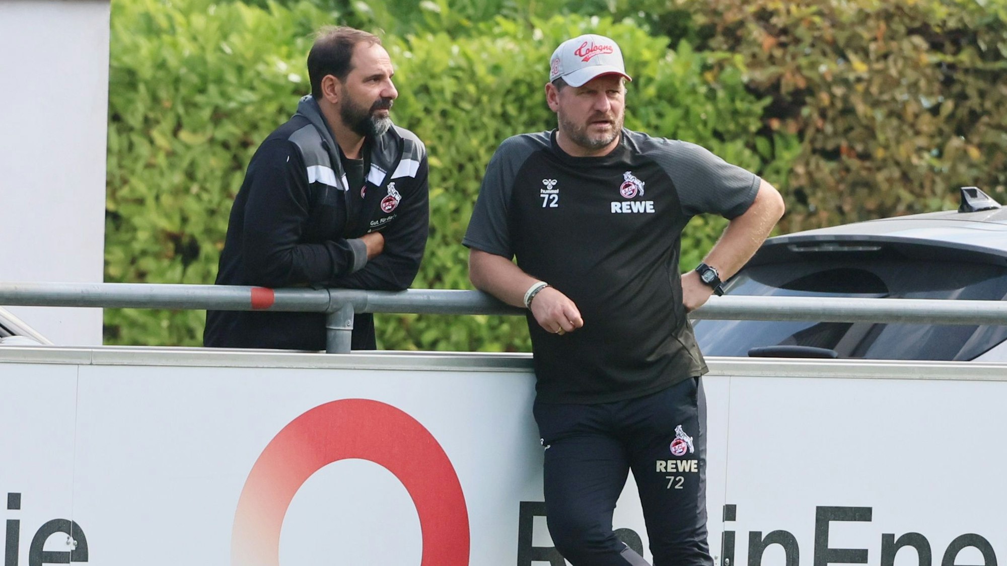 U19-Trainer Stefan Ruthenbeck unterhält sich mit Profi-Coach Steffen Baumgart am Geißbockheim an der Bande.