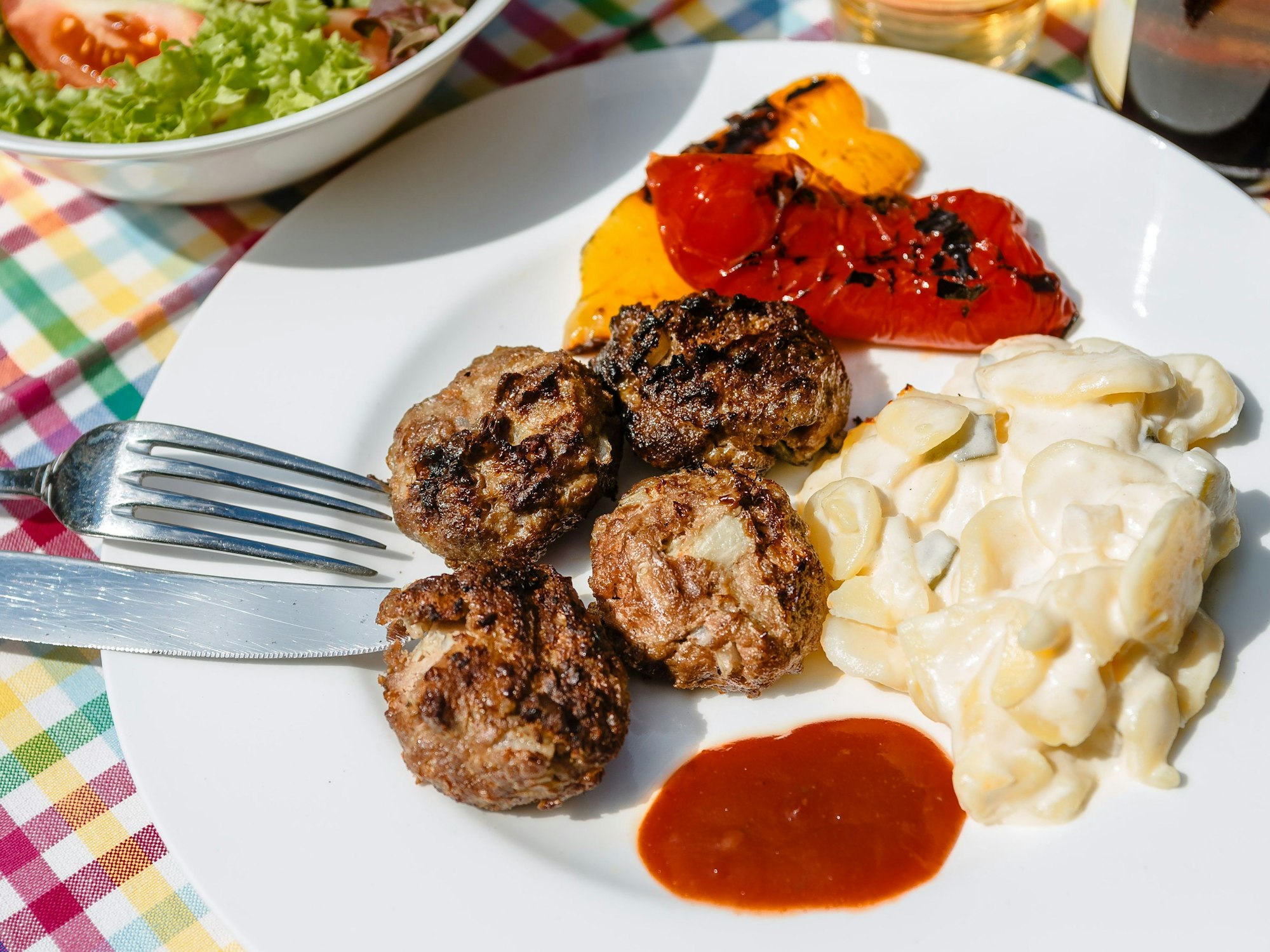 Das Foto zeigt einen Teller mit Fleischbällchen und Kartoffelsalat auf einer bunt-karierten Tischdecke.