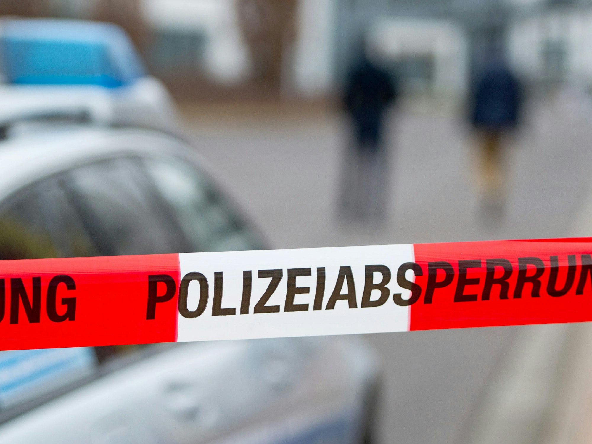 Ein Polizeiabsperrband ist vor einem Polizeiwagen zu sehen.