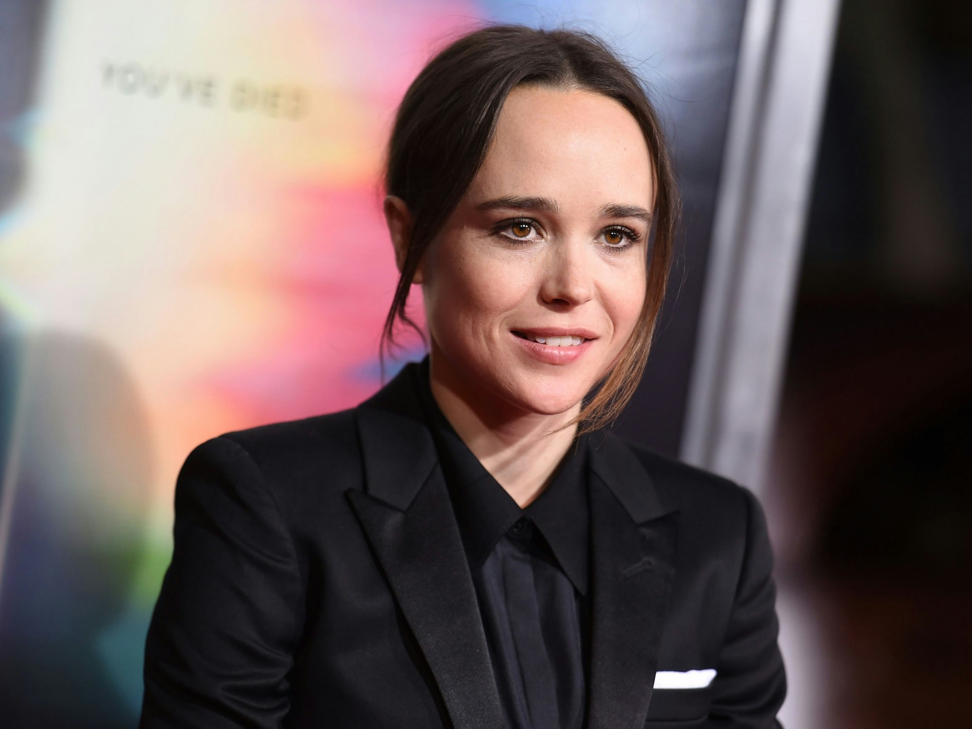 Das Foto aus dem Jahr 2017 zeigt den Trans-Schauspieler Elliot Page, der sich damals noch als Ellen Page identifizierte. Die Person auf dem Foto trägt einen schwarzen Anzug und hat die Haare zu einem Zopf gebunden.