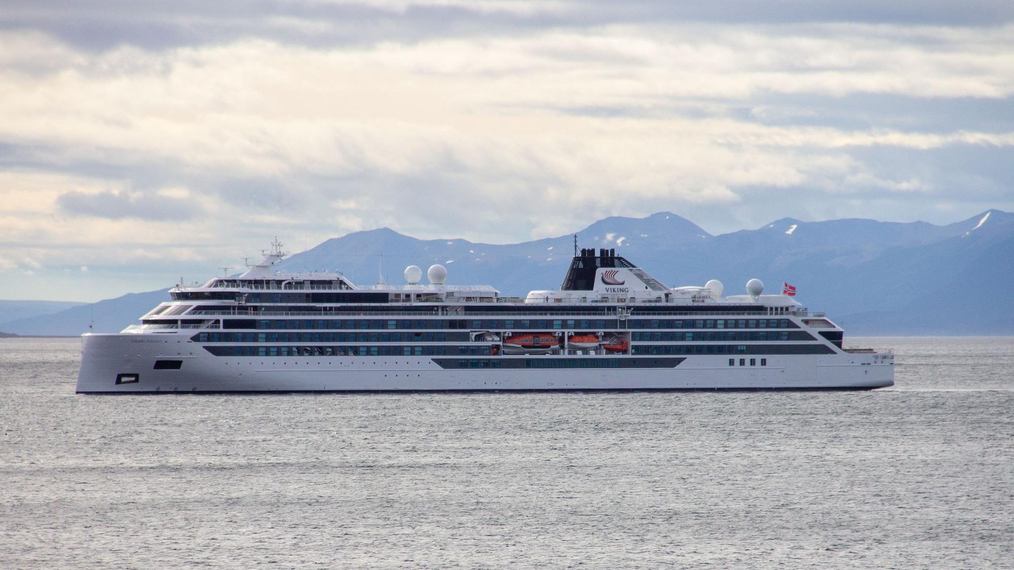 Das Foto aus dem Jahr 2022 zeigt ein Kreuzfahrtschiff auf offenem Meer. Im Hintergrund ragen Berge in den wolkigen Himmel empor.