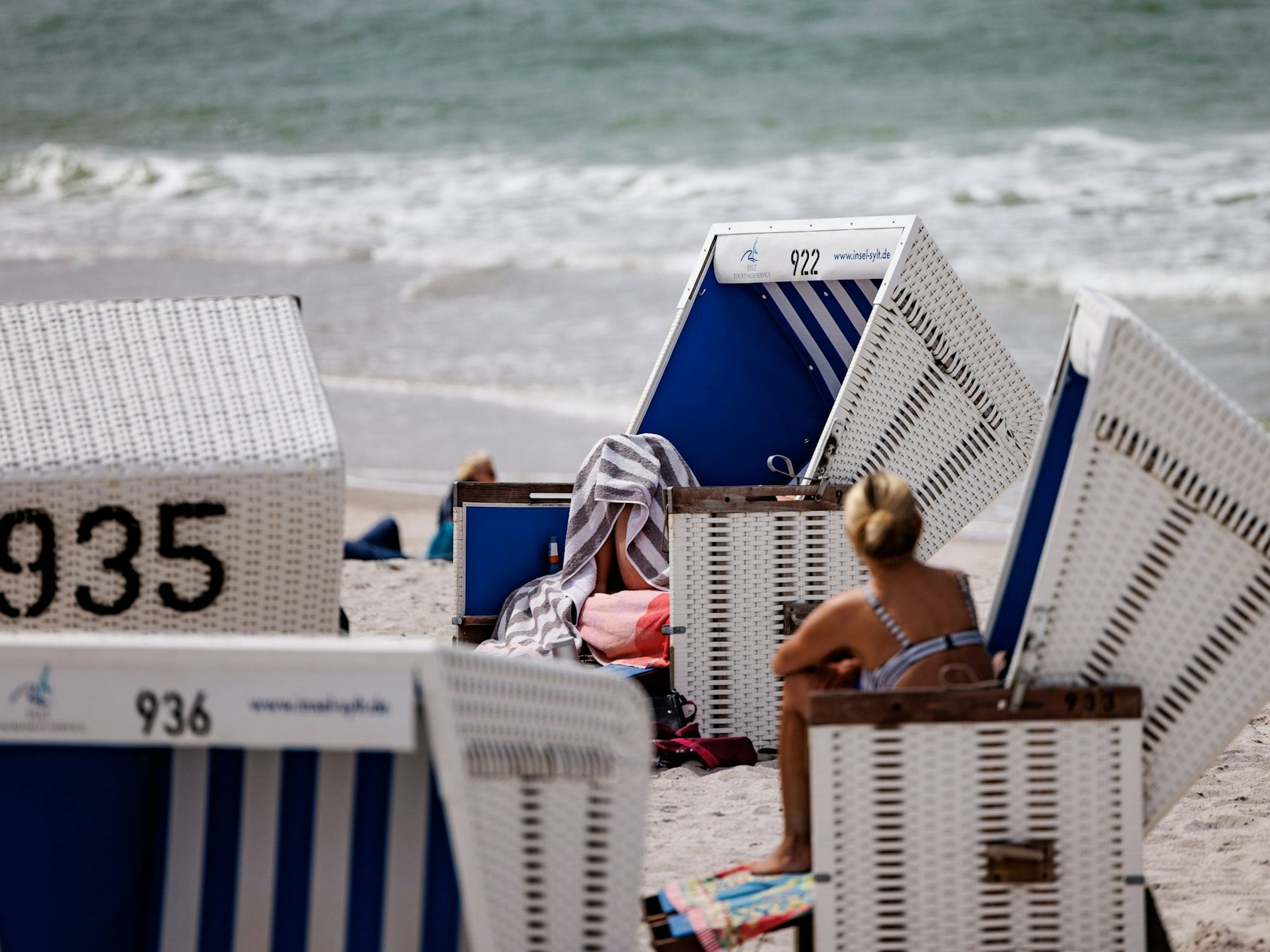 Das Foto aus dem Jahr 2022 zeigt mehrere weiß-blaue Strandkörbe am Sylter Strand. Im Hintergrund schlagen Wellen der Nordsee ans Ufer.